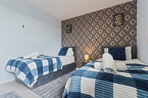 A hotel room with two beds, a patterned wall, and a small table with a lamp. - Retreat Private Rooftop 3 Bedroom Apartment (London)
