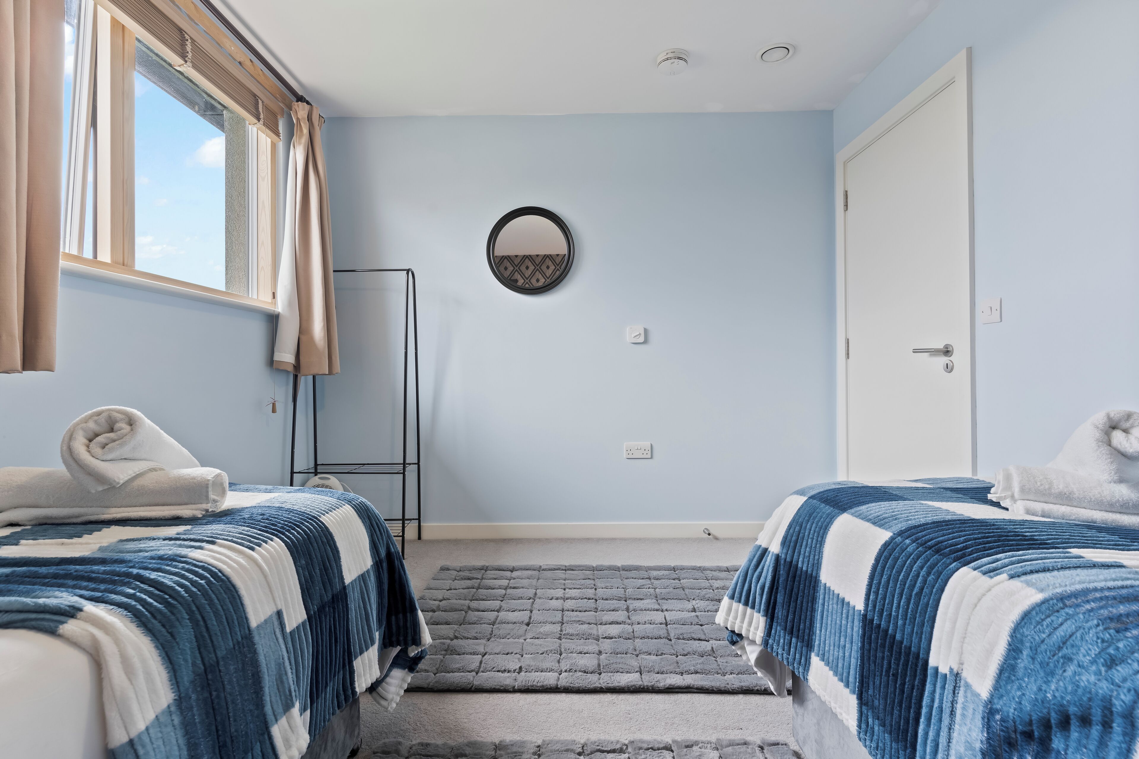 Een kamer met twee bedden, een raam met gordijnen, een ronde spiegel en een deur.