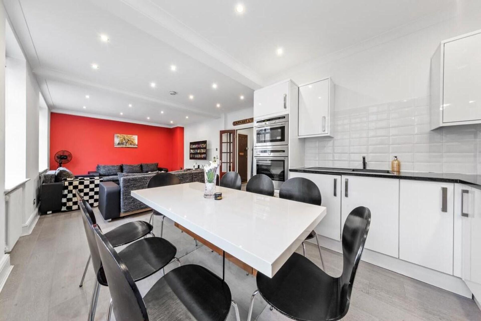 A modern kitchen with white cabinets, a dining table with chairs, and a red accent wall.