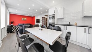 A modern kitchen with white cabinets, a dining table with chairs, and a red accent wall. - London Chic Apartment - City Center Gem (London)
