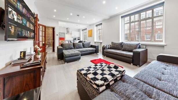 A modern living room with two sofas, a coffee table, and a TV mounted on the wall displaying a movie. - London Chic Apartment - City Center Gem (London)