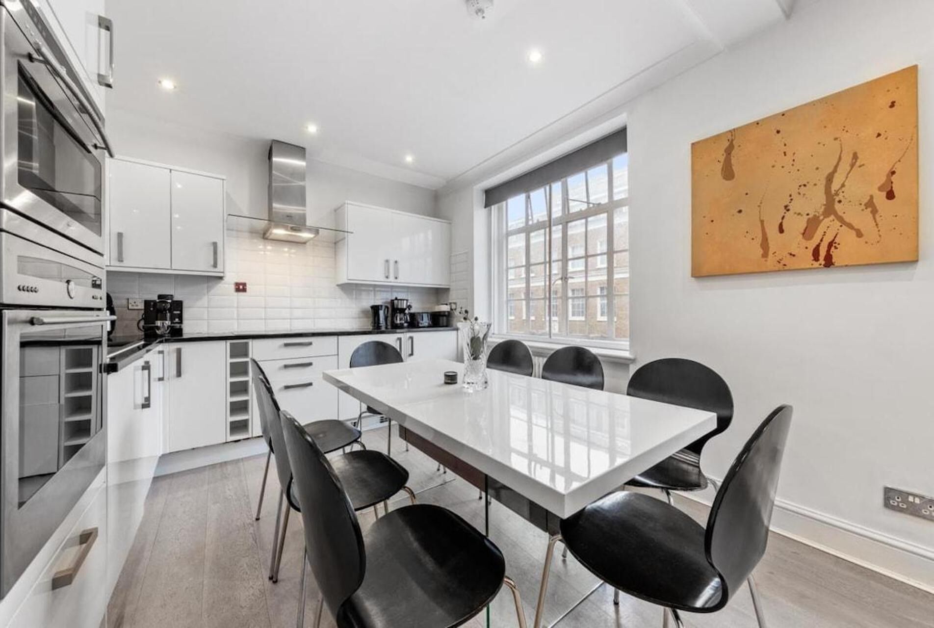 A modern kitchen with white cabinets, a large island, and black chairs.