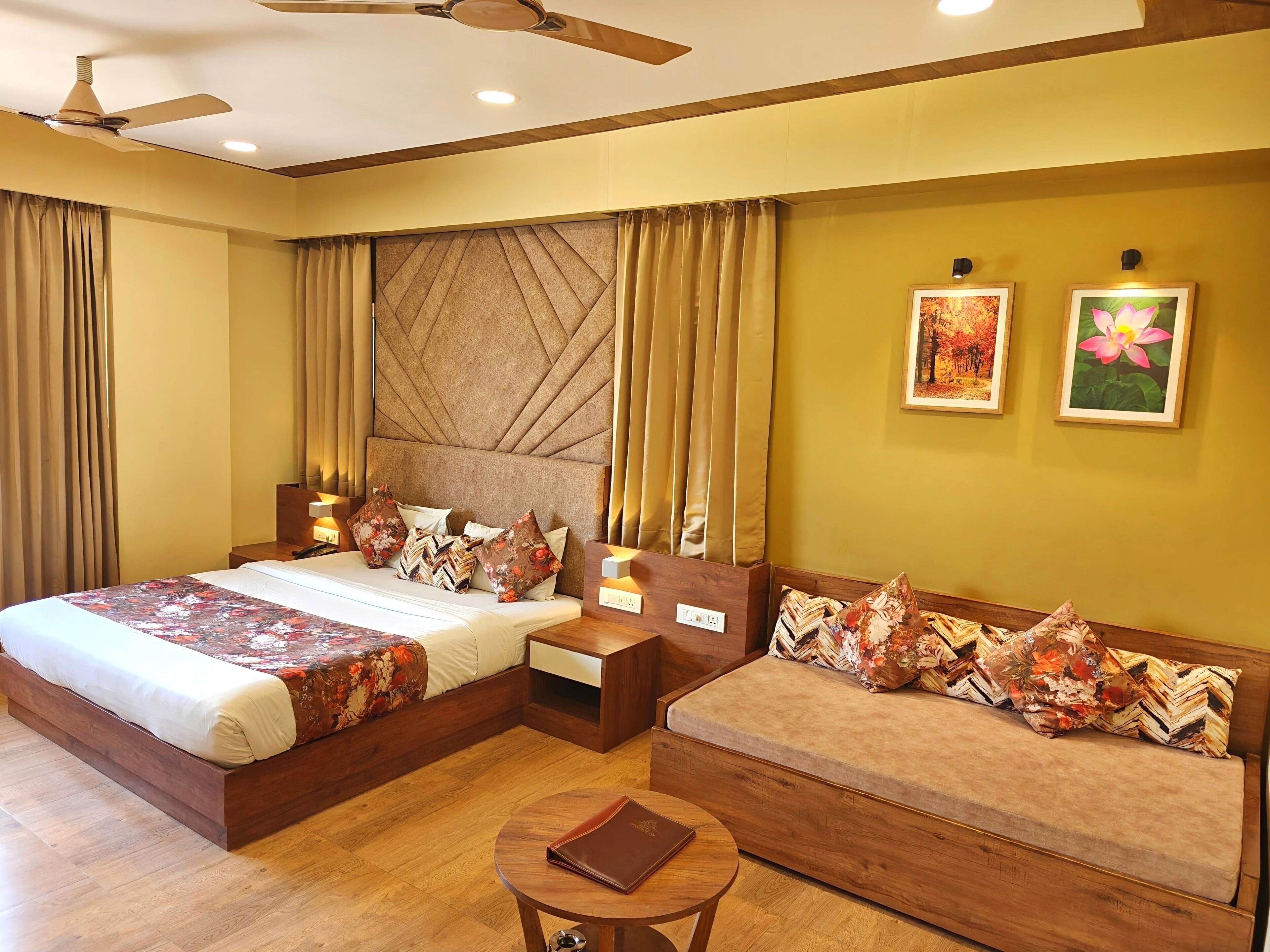 A hotel room with a large bed, a sofa, a small table, and a ceiling fan.