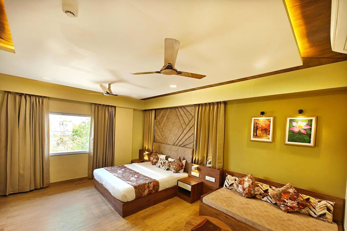 A modern hotel room with a large bed, a sofa, a small table, and a ceiling fan.