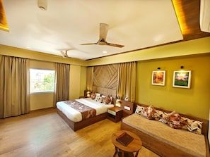 A modern hotel room with a large bed, a sofa, a small table, and a ceiling fan. - Hotel Opulence Inn (Udaipur)