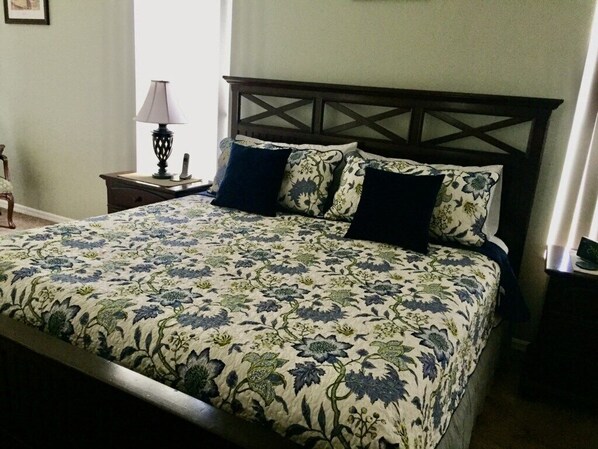 A neatly made bed with a floral bedspread, a wooden headboard, and a bedside table with a lamp. - Hampton Lakes Villa (Davenport)
