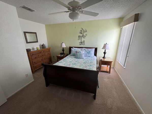 A bedroom with a bed, two nightstands, a dresser, a ceiling fan, and a window with blinds.