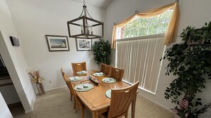 A dining area with a wooden table set for six, surrounded by chairs, a chandelier, and framed pictures on the wall. - Julliard Villa (Davenport)