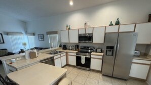 A modern kitchen with a central island, stainless steel appliances, and a tiled floor. - Julliard Villa (Davenport)