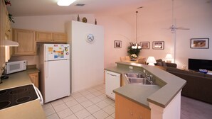 A compact kitchen with a microwave, refrigerator, stove, and a dining area with a table and chairs. - Cumbrian Retreat (Kissimmee)