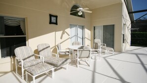 A sunlit patio with white furniture, including chairs and a table, and a ceiling fan. - Cumbrian Retreat (Kissimmee)