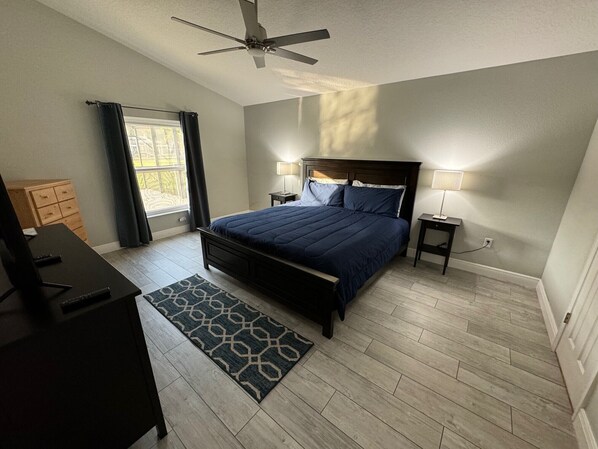 A bedroom with a bed, a desk, a ceiling fan, and a window with curtains.