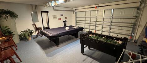 A room with a pool table, a foosball table, and a garage door.