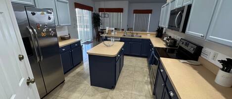 A modern kitchen with a central island, stainless steel appliances, and blue cabinetry.