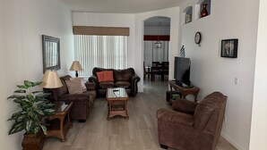 Ein Wohnzimmer mit einer Couch, Sesseln, einem Couchtisch, einem Fernseher und einem Essbereich mit Tisch und Stühlen.