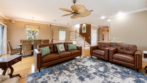 A spacious living room with a brown leather sofa, a blue patterned rug, and a ceiling fan. - Gigi & Poppy’s Paradise: Pool, Gulf Views, Walk to Beach (Holmes Beach)
