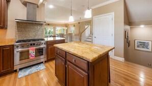 A kitchen with wooden cabinets, a granite countertop, stainless steel appliances, and a tiled backsplash. - Gigi & Poppy’s Paradise: Pool, Gulf Views, Walk to Beach (Holmes Beach)