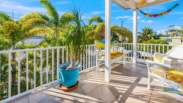 A covered outdoor area with a white railing, a blue potted plant, a white sofa with yellow cushions, and a ceiling fan with a bee design. - Gigi & Poppy’s Paradise: Pool, Gulf Views, Walk to Beach (Holmes Beach)
