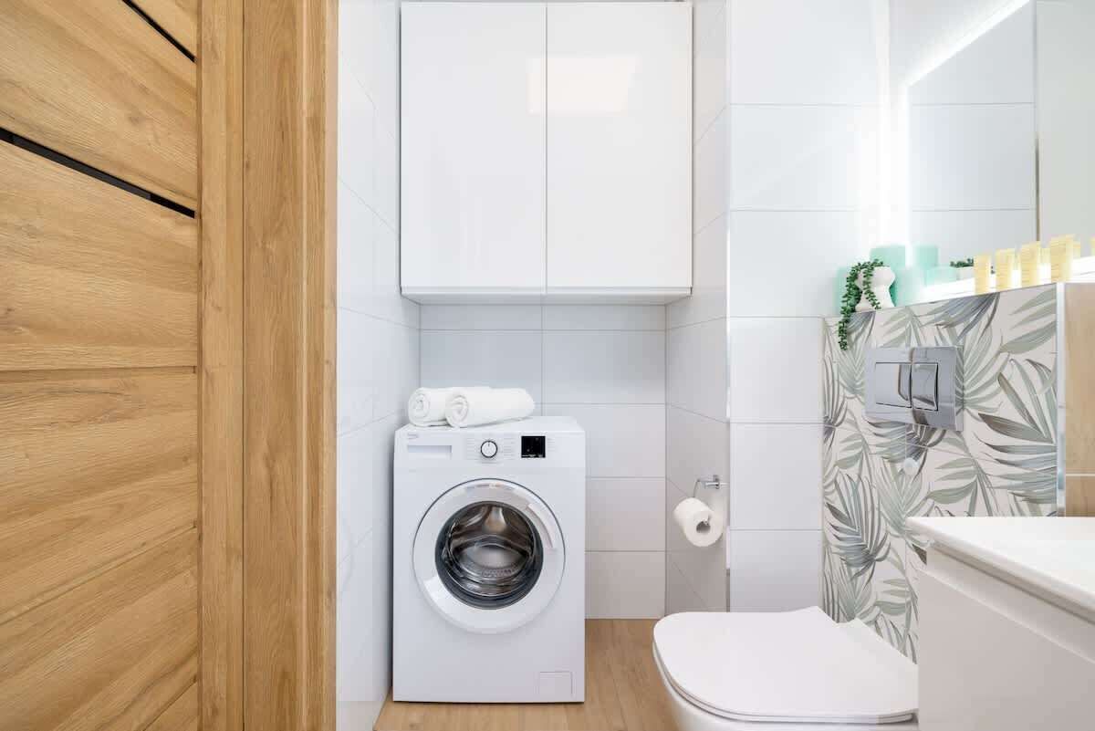 Un baño pequeño con lavadora, inodoro y un armario sobre la lavadora.