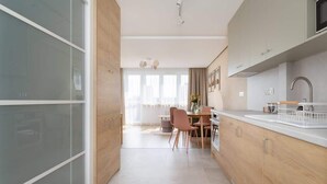 A modern kitchen with wooden cabinets, a dining area with a table and chairs, and a view of the living room through a glass door. - Stylish Apartment in the Center | Air Conditioning, Balcony (Katowice)