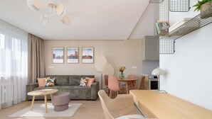 A modern living room with a sofa, coffee table, and dining area. There are framed pictures on the wall, a kitchen area, and a staircase with a shelf. - Stylish Apartment in the Center | Air Conditioning, Balcony (Katowice)