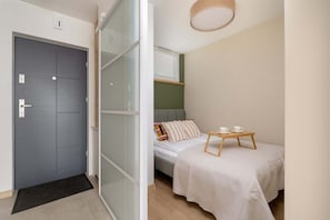 Une petite chambre à coucher moderne, avec un lit, une table de chevet et une porte donnant sur une autre pièce.