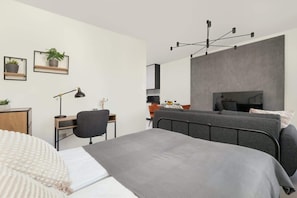 A modern bedroom with a bed, desk, chair, and a hanging light fixture.