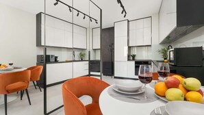 Eine moderne Küche mit weißen Schränken, ein Essbereich mit orangefarbenen Stühlen und ein Tisch gedeckt mit Tellern, Gläsern und Obst.