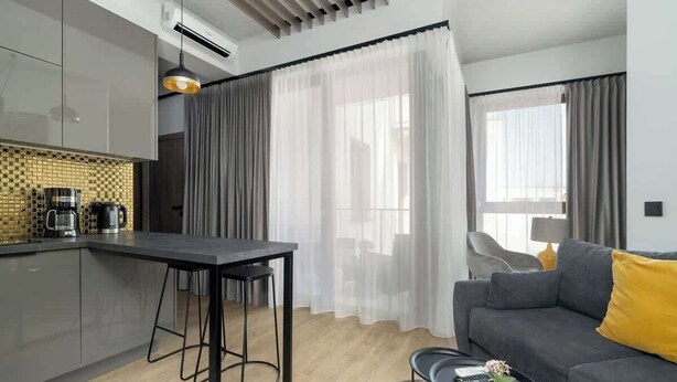 A modern kitchen with a bar area, a grey sofa with yellow cushions, and a small round table with a plant. - Stylish Studio in the Center | Air Conditioning, Balcony (Poznan)