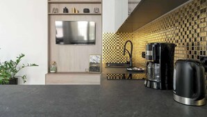 A modern kitchen with a flat-screen TV mounted on a wooden wall, a coffee maker, and a kettle on the counter. - Stylish Studio in the Center | Air Conditioning, Balcony (Poznan)