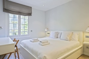Um quarto com cama, mesas de cabeceira, escrivaninha e uma cadeira.