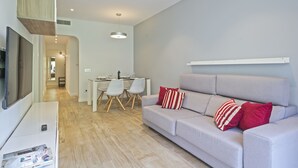 Een moderne woonkamer met een grijze bank, een flatscreen televisie en een eethoek met een tafel en stoelen.