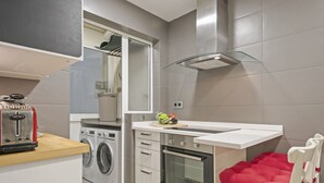 Een compacte keuken met een wasmachine, oven en een klein eethoekje met een stoel.