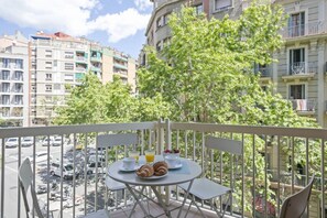 Varanda com mesa posta para o café da manhã, com vista para uma rua com carros estacionados e edifícios.
