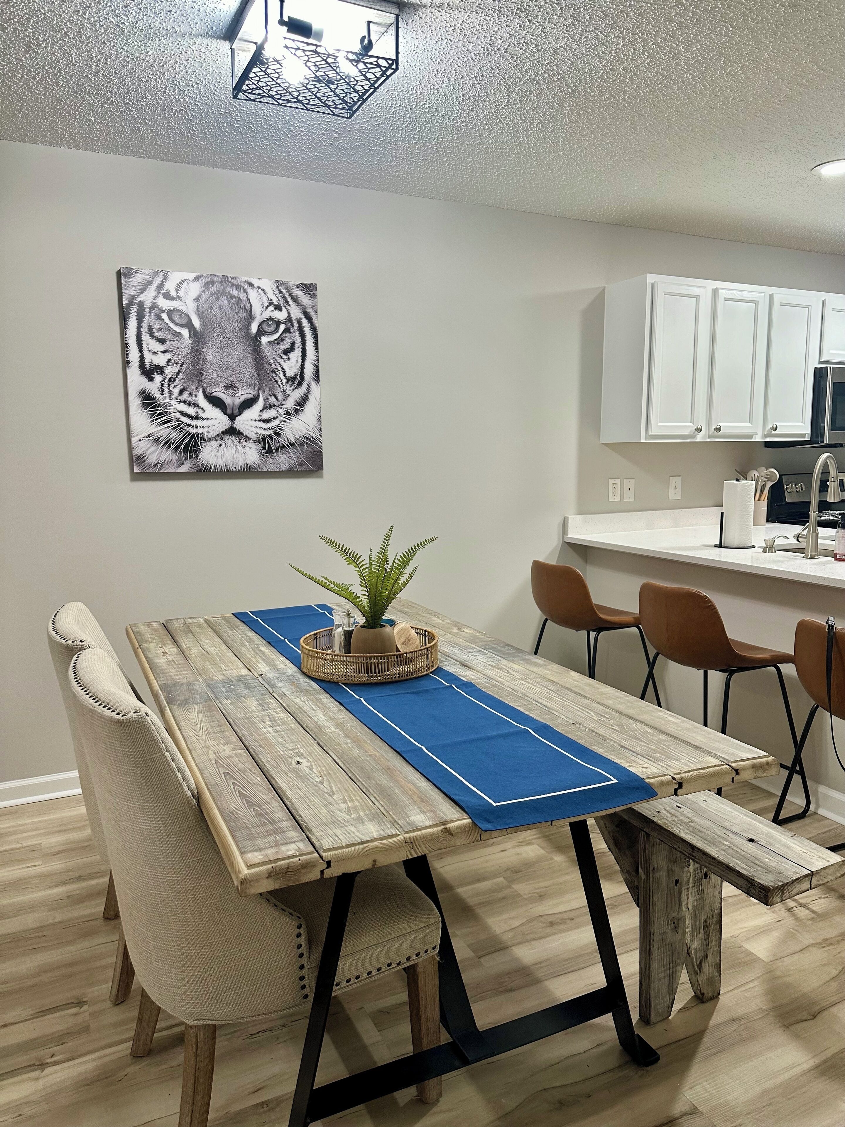 A dining area with a wooden table, blue placemat, and chairs. A tiger artwork is on the wall.