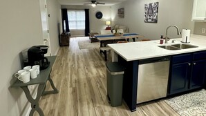 Una cocina moderna con una isla central, un área de comedor con sofá y una sala de estar con televisor.