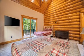 Un dormitorio de cabaña de madera con cama, cómoda, televisor montado en la pared y puerta corrediza de vidrio que da a un balcón exterior.