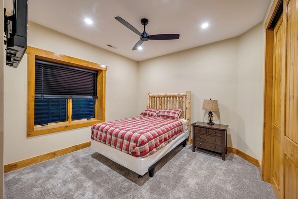 Un dormitorio con cama, mesita de noche, lámpara, ventilador de techo y ventana con persianas.