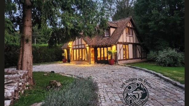 Une maison traditionnelle à colombages, avec un toit de chaume, une allée pavée et un jardin bien entretenu.