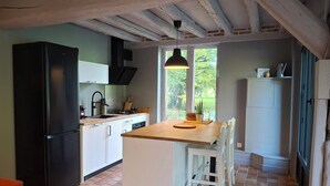 Une cuisine avec un réfrigérateur noir, des armoires blanches, un îlot central en bois et un luminaire suspendu.