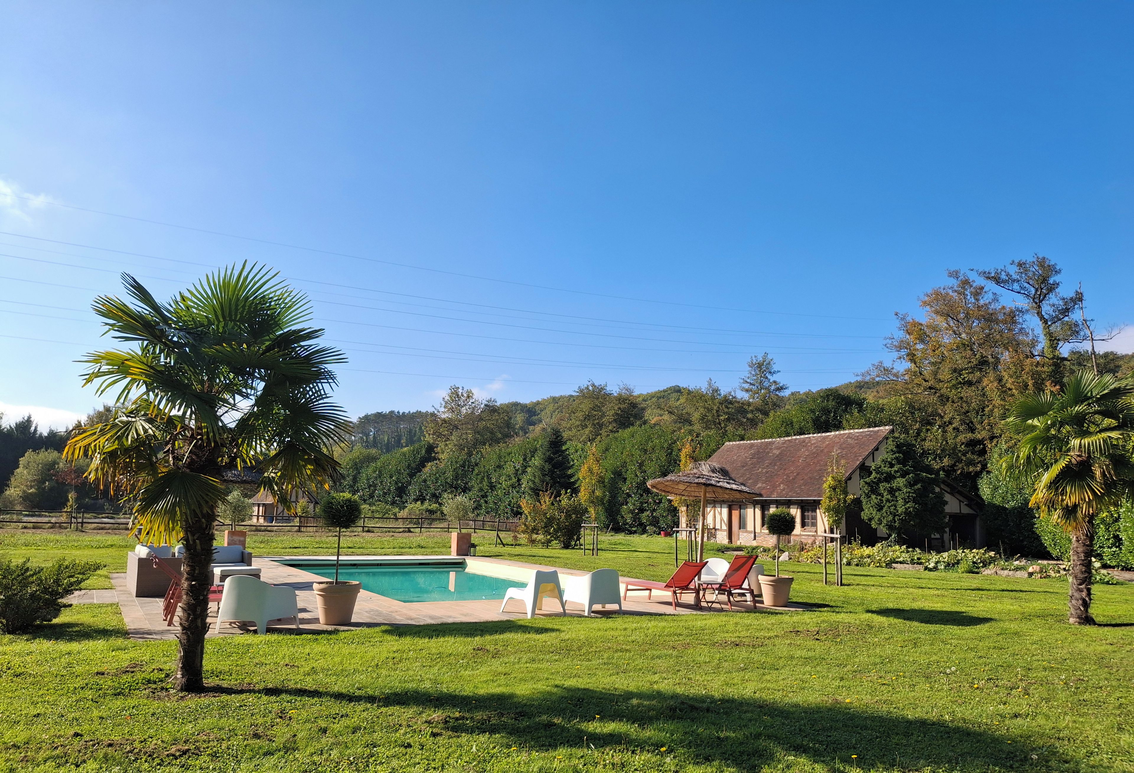 Un área de piscina con sillones de descanso y una casa al fondo.