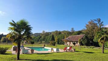 Un área de piscina con sillones de descanso y una casa al fondo.