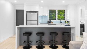 Una cocina moderna con una isla central, taburetes de bar, un refrigerador y una ventana con follaje.