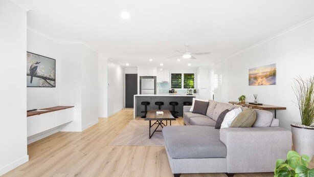 Una sala de estar moderna con un sofá gris, una mesa de comedor y una cocina al fondo.