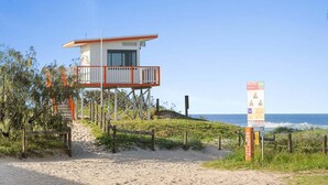 Una torre de socorrista con balcón, una playa arenosa y un cartel con información de seguridad.