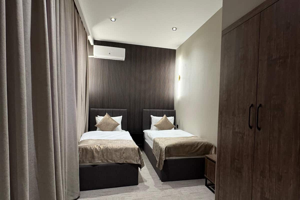 A hotel room with two beds, a wardrobe, and a ceiling-mounted air conditioner.