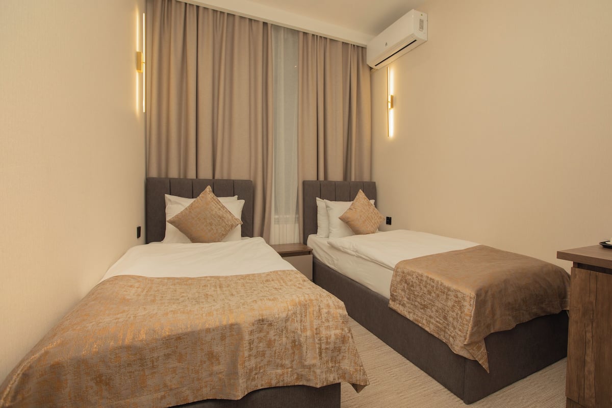 A hotel room with two beds, a nightstand, and an air conditioning unit.