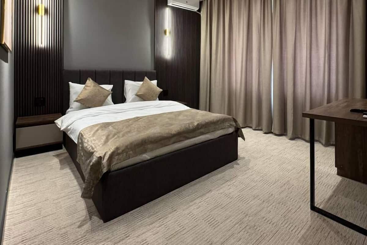 A modern bedroom with a large bed, dark headboard, and a desk with a chair.