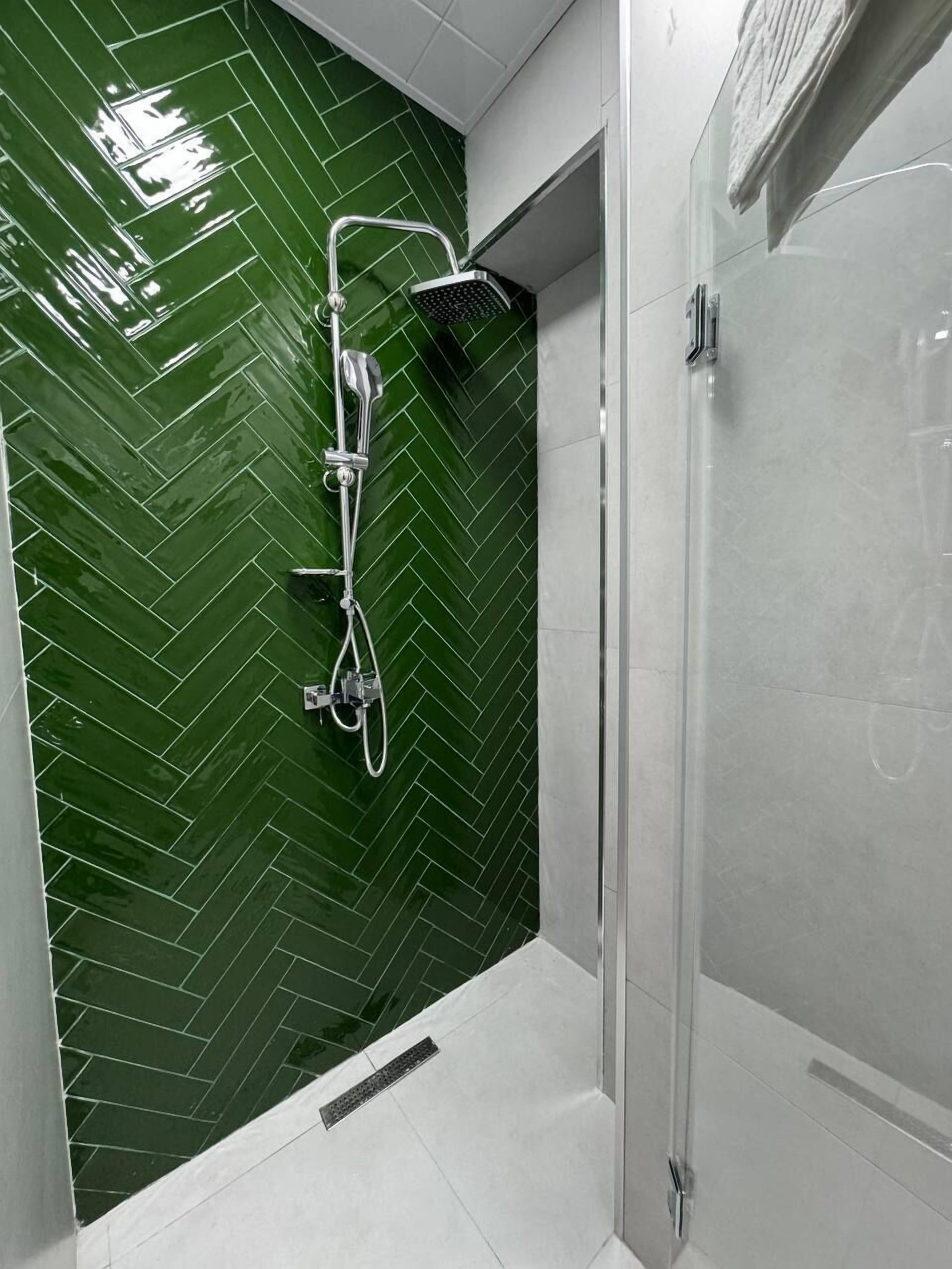 A modern bathroom with a green herringbone tile backsplash, a shower with a handheld showerhead, and a glass shower enclosure.