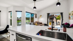 A modern kitchen with a large island, a dining area with a black chair, and a view of a pool and mountains. - Beautifully Updated 2 Bedroom Condo with Stunning Views (La Quinta)